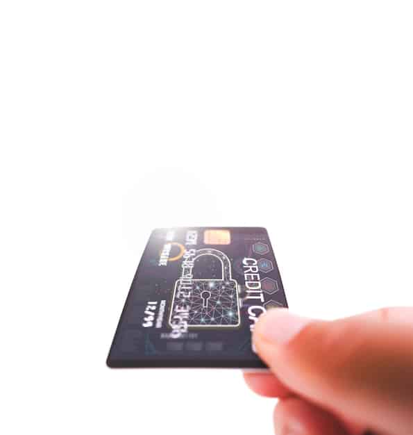 A detailed close-up of a hand holding a credit card, emphasizing the numbers and security features, with a blurred background of a modern bank interior. The focus is on the credit card to signify consumer finance.